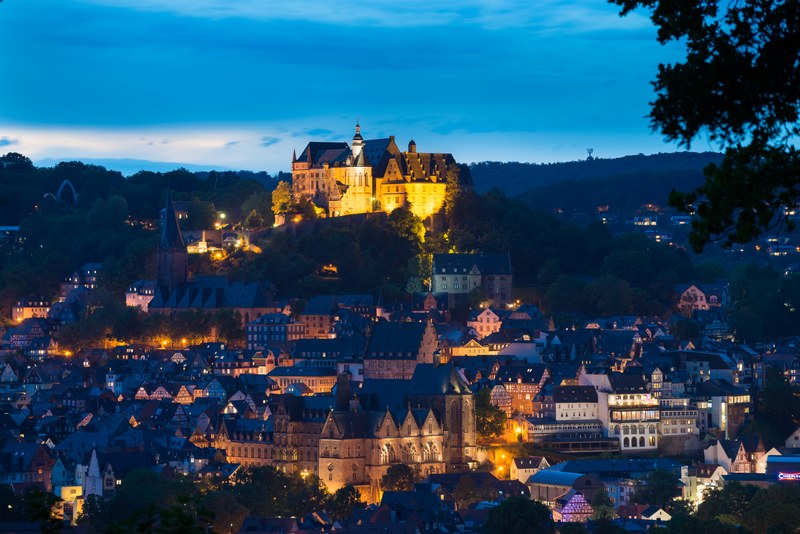 Stadtansicht von Marburg im blauen Abendlicht. Schloss, Alte Universität und Oberstadt sind beleuchtet.